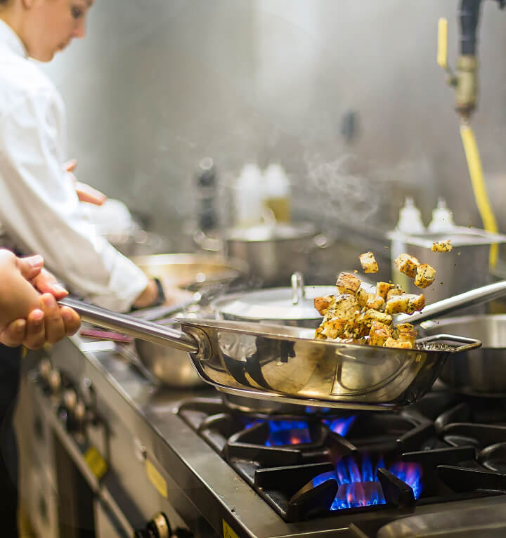 A chef tosses herb-seasoned potatoes in a skillet over a hot flame at a restaurant kitchen