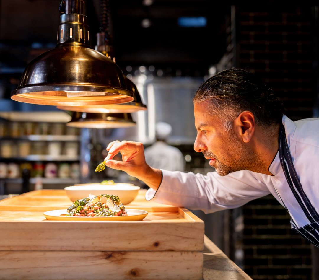 A male chef is finishing a gourmet plate of food in a restaurant kitchen
