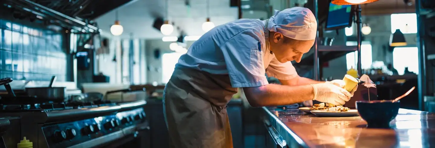 A male chef finishes a dish in a restaurant kitchen