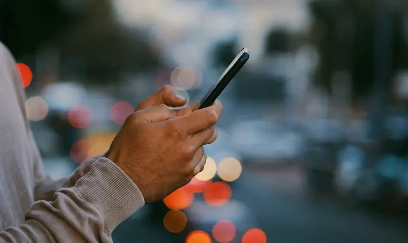 Close-up of a person's hands while they are scrolling on their phone outside. 