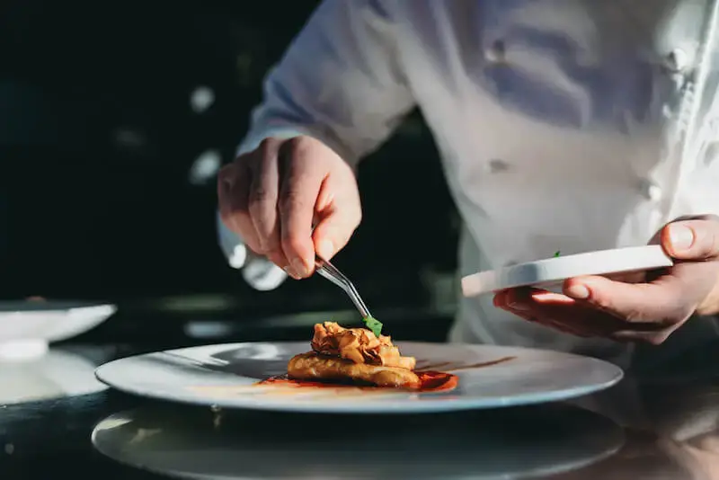 Culinary professional plating dish with precision in restaurant kitchen.