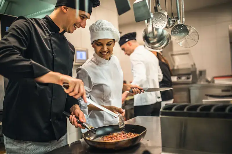Professional kitchen team of diverse cooks collaborating together during food preparation in modern restaurant kitchen.