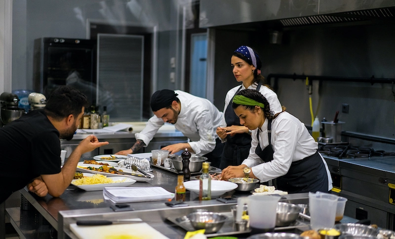 A group of culinary team members examining plated dishes together in a professional kitchen.